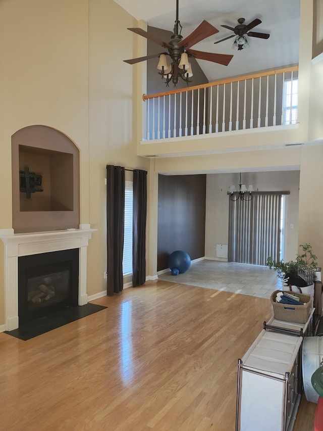 unfurnished living room featuring a towering ceiling, ceiling fan with notable chandelier, and hardwood / wood-style floors