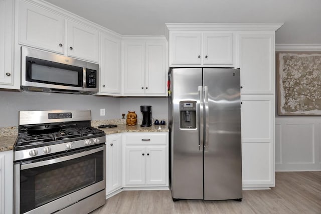 kitchen with light stone counters, white cabinets, stainless steel appliances, and light wood-type flooring