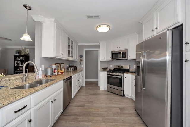 kitchen with pendant lighting, white cabinets, sink, light hardwood / wood-style flooring, and stainless steel appliances