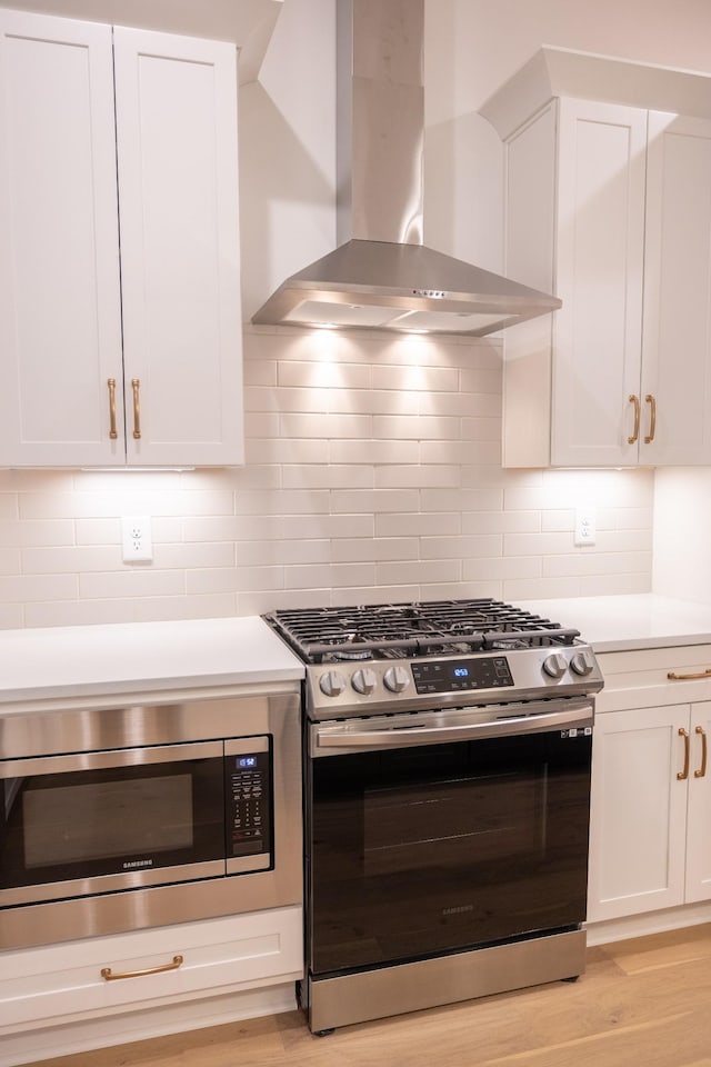 kitchen featuring wall chimney exhaust hood, light hardwood / wood-style floors, white cabinetry, and stainless steel appliances