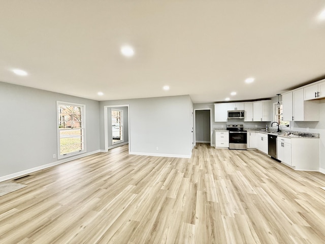 kitchen with light countertops, appliances with stainless steel finishes, open floor plan, white cabinets, and a sink