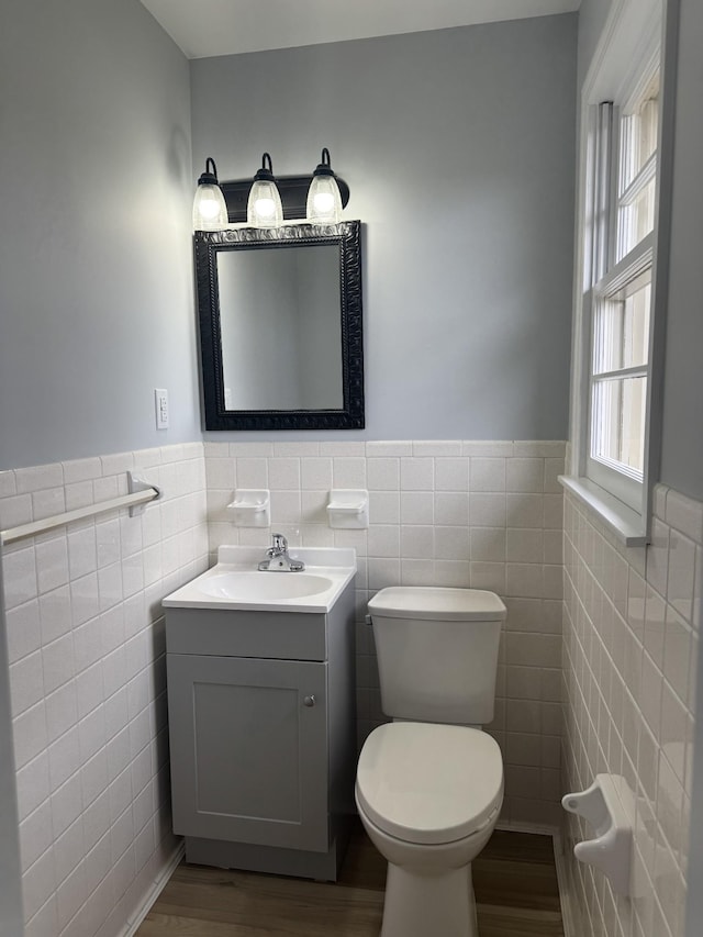 half bathroom featuring a wainscoted wall, tile walls, toilet, vanity, and wood finished floors