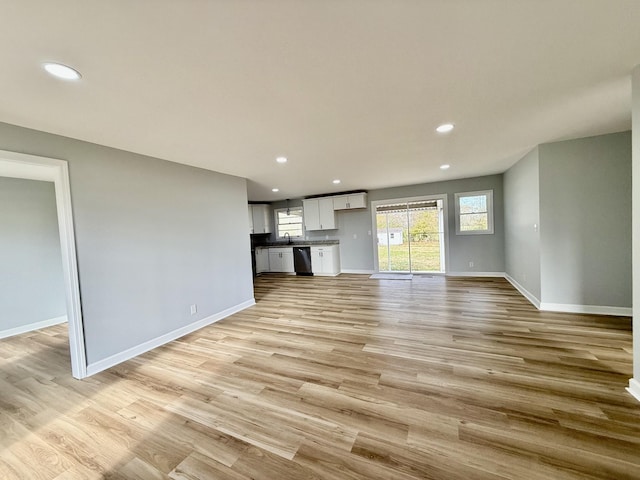 unfurnished living room with baseboards, light wood-type flooring, a sink, and recessed lighting