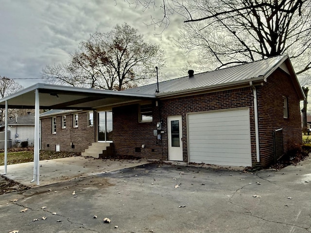 rear view of property featuring metal roof, a garage, brick siding, driveway, and a carport