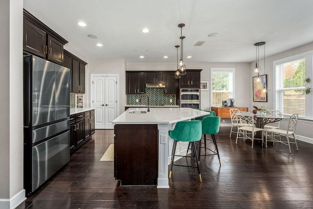 kitchen featuring dark hardwood / wood-style flooring, a center island with sink, hanging light fixtures, and appliances with stainless steel finishes