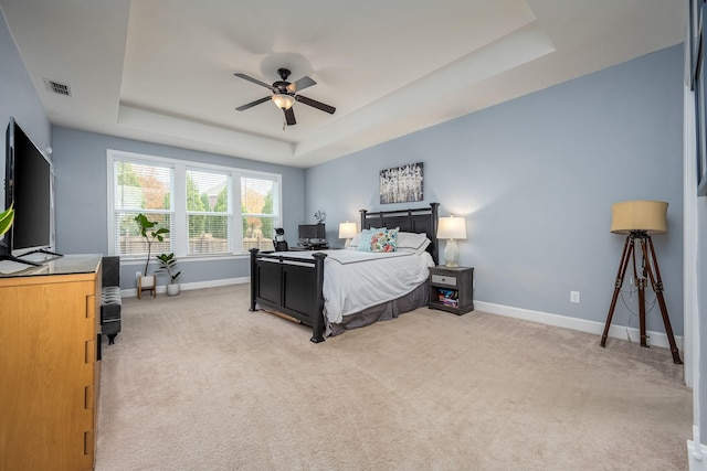 bedroom with a raised ceiling, ceiling fan, and light colored carpet