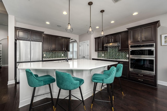 kitchen featuring a large island with sink, decorative light fixtures, and dark wood-type flooring