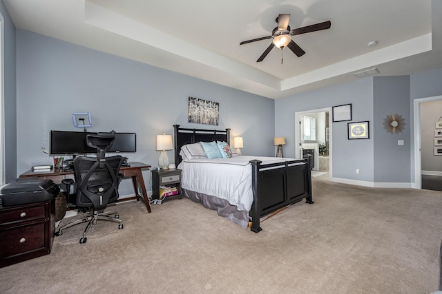 bedroom with a raised ceiling, ceiling fan, light colored carpet, and connected bathroom