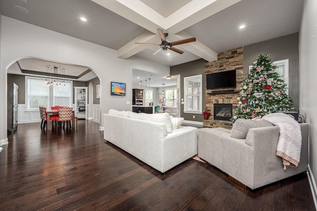 living room with beam ceiling, a healthy amount of sunlight, a stone fireplace, and dark wood-type flooring