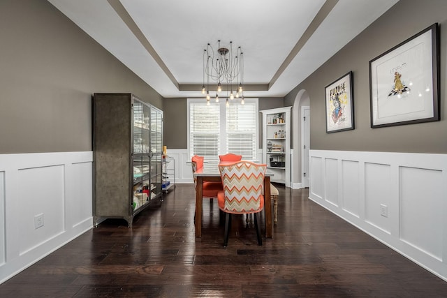 dining space featuring a raised ceiling, dark wood-type flooring, and a notable chandelier