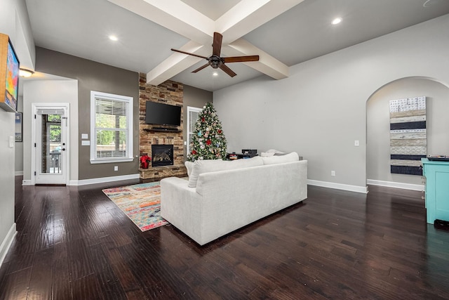 living room featuring ceiling fan, a fireplace, beamed ceiling, and dark wood-type flooring