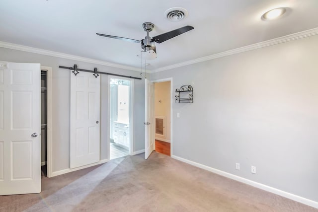 spare room featuring ceiling fan, a barn door, ornamental molding, and light carpet