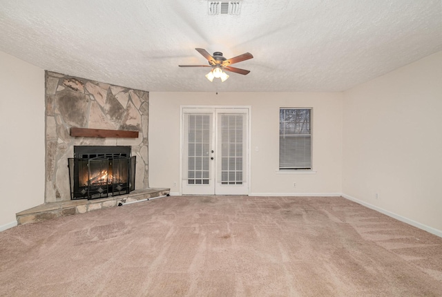 unfurnished living room featuring carpet flooring, ceiling fan, french doors, a stone fireplace, and a textured ceiling