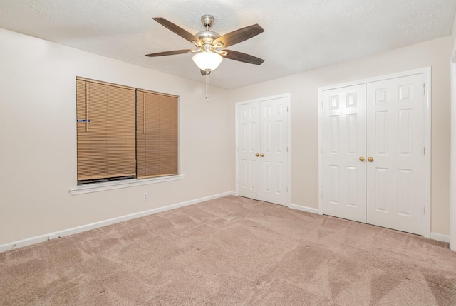 unfurnished bedroom featuring ceiling fan, light carpet, and two closets