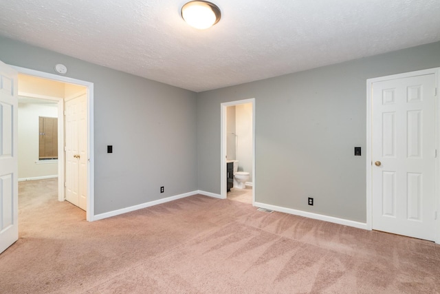 unfurnished bedroom with light carpet, a textured ceiling, ensuite bath, and a closet