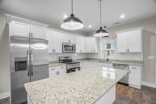 kitchen with hanging light fixtures, appliances with stainless steel finishes, a sink, and white cabinetry