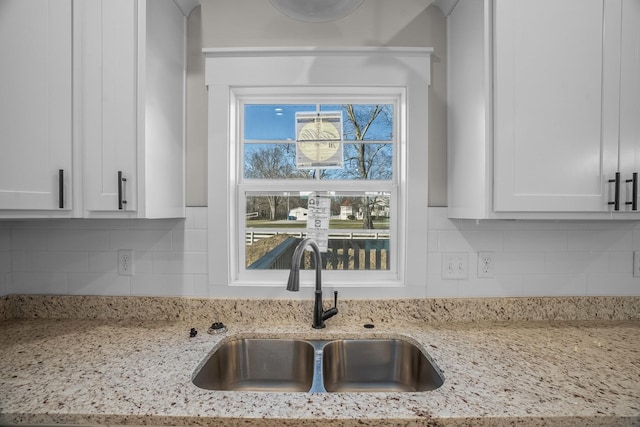 kitchen with light stone countertops, tasteful backsplash, white cabinetry, and a sink