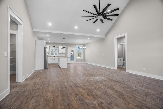 unfurnished living room featuring dark wood-type flooring, high vaulted ceiling, baseboards, and ceiling fan with notable chandelier