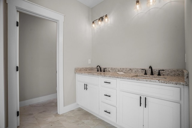 bathroom with double vanity, marble finish floor, baseboards, and a sink