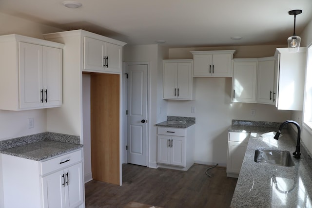 kitchen featuring dark wood-type flooring, stone counters, sink, decorative light fixtures, and white cabinetry