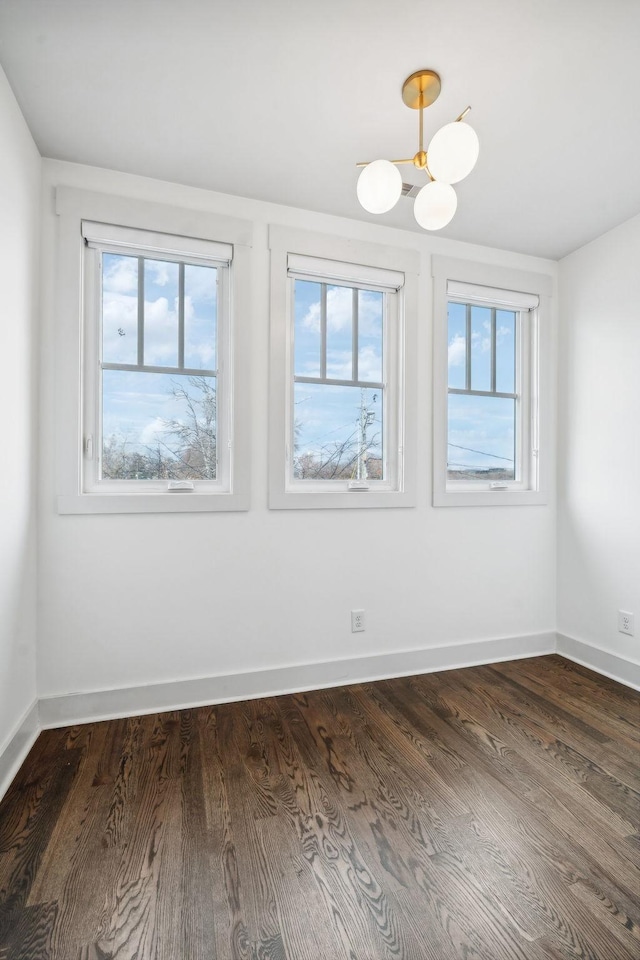 unfurnished room with dark hardwood / wood-style floors, a healthy amount of sunlight, and an inviting chandelier