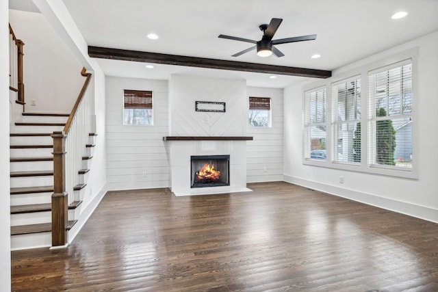 unfurnished living room featuring beamed ceiling, ceiling fan, a large fireplace, and dark hardwood / wood-style flooring