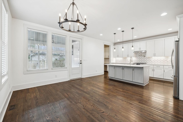 kitchen featuring pendant lighting, white cabinetry, dark hardwood / wood-style floors, stainless steel refrigerator, and an island with sink