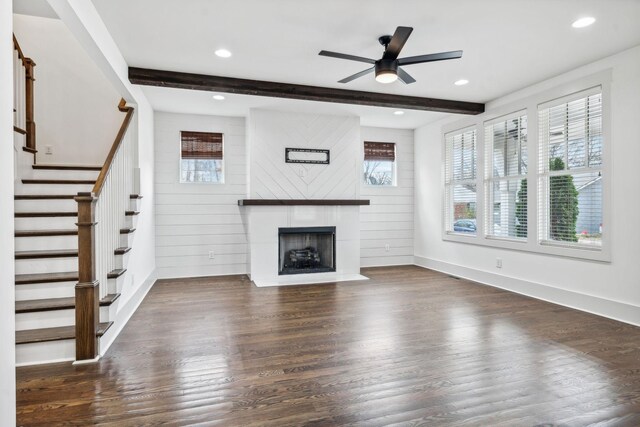 unfurnished living room featuring wood walls, ceiling fan, a fireplace, beam ceiling, and dark hardwood / wood-style flooring