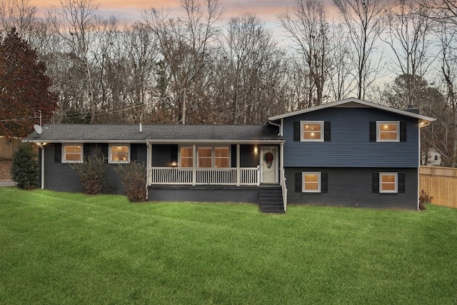 back house at dusk featuring covered porch and a yard