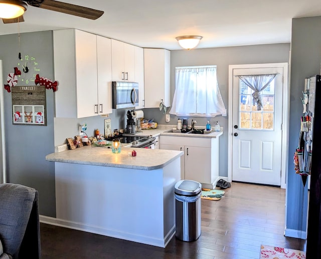 kitchen with kitchen peninsula, dark hardwood / wood-style floors, stainless steel appliances, white cabinets, and sink