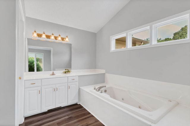 bathroom with wood-type flooring, vanity, vaulted ceiling, and a tub