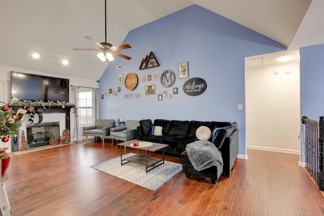 living room with hardwood / wood-style floors, ceiling fan, a fireplace, and high vaulted ceiling