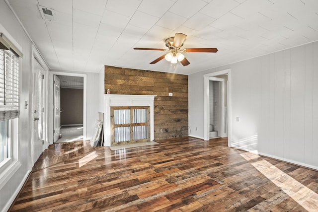 unfurnished living room featuring dark hardwood / wood-style flooring, plenty of natural light, wooden walls, and ceiling fan