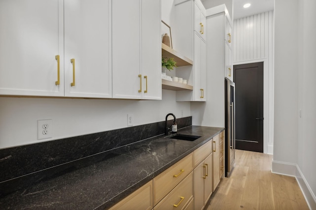 kitchen featuring white cabinets, light wood-type flooring, sink, and dark stone counters