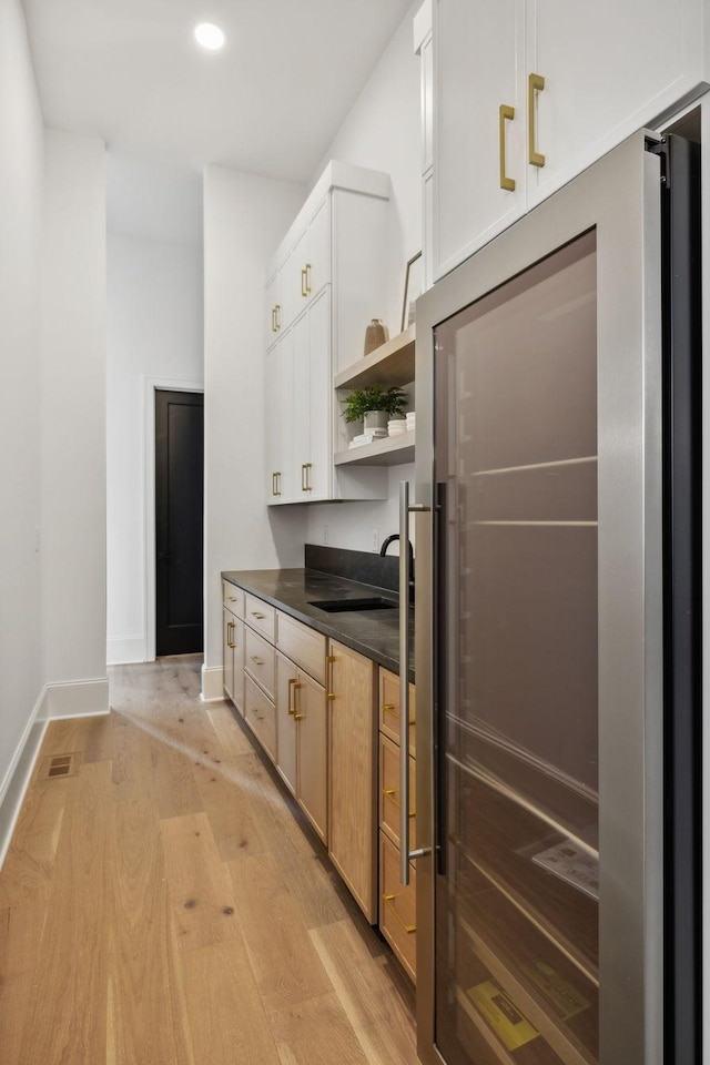 kitchen with high end refrigerator, sink, light brown cabinets, light hardwood / wood-style floors, and white cabinetry