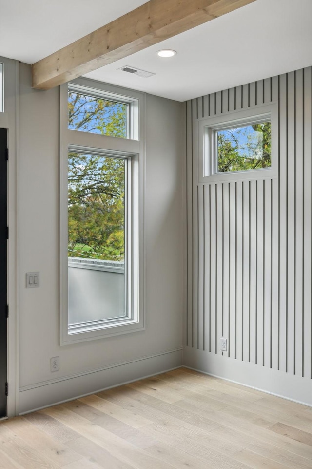 unfurnished room with beam ceiling, light hardwood / wood-style flooring, and a wealth of natural light