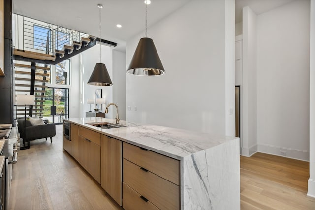 kitchen featuring light stone countertops, an island with sink, light hardwood / wood-style floors, and sink