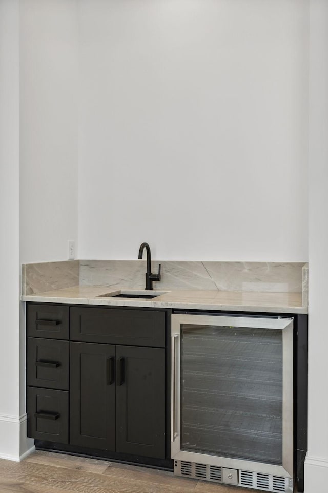 bar featuring sink, beverage cooler, and light hardwood / wood-style flooring