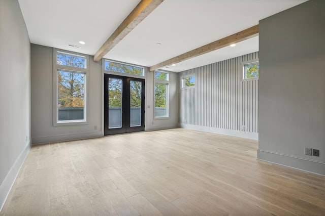 empty room with beam ceiling, a wealth of natural light, french doors, and light hardwood / wood-style floors