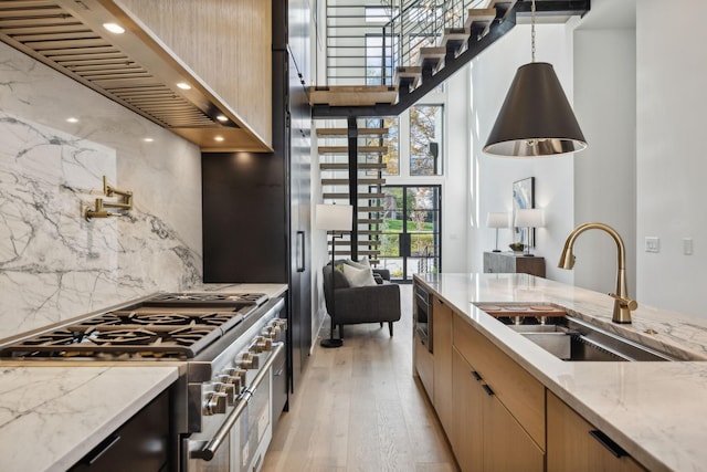 kitchen with sink, backsplash, light hardwood / wood-style floors, decorative light fixtures, and appliances with stainless steel finishes