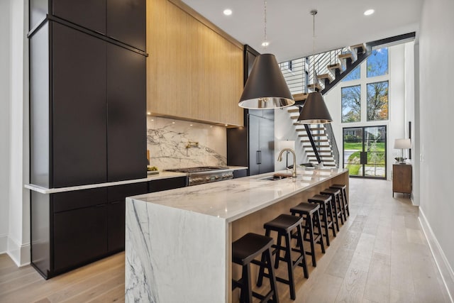 kitchen featuring sink, stainless steel gas cooktop, decorative backsplash, a center island with sink, and light wood-type flooring