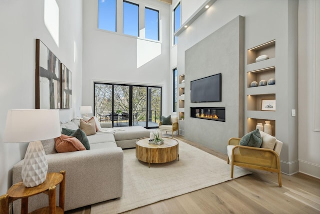 living room featuring built in shelves, a towering ceiling, a fireplace, and light hardwood / wood-style flooring