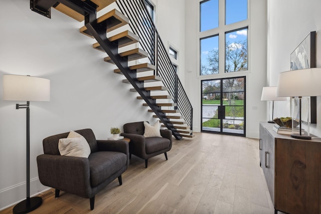 sitting room with light wood-type flooring and a towering ceiling