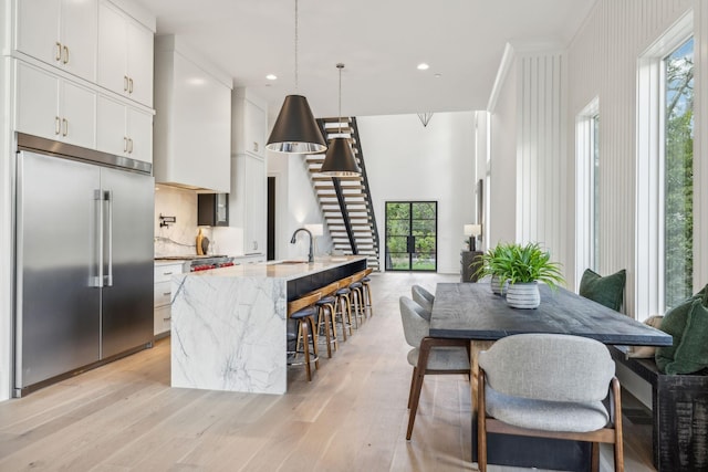 kitchen with hanging light fixtures, built in fridge, a center island with sink, and light stone counters