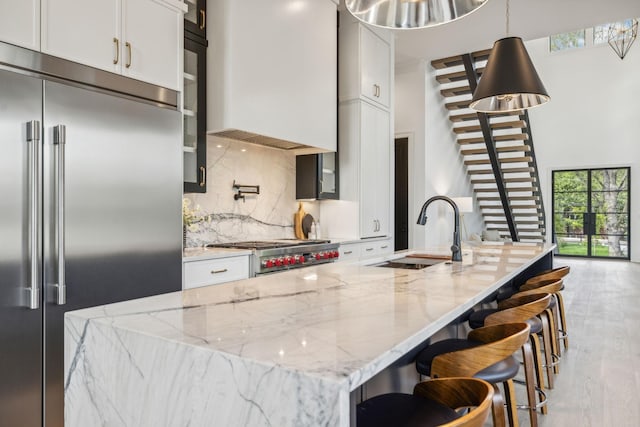 kitchen featuring white cabinetry, sink, light stone countertops, stainless steel built in refrigerator, and a kitchen island with sink