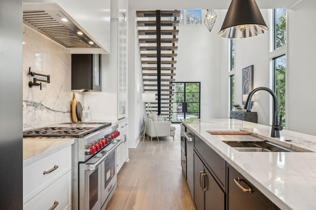 kitchen with sink, wall chimney range hood, tasteful backsplash, double oven range, and white cabinets