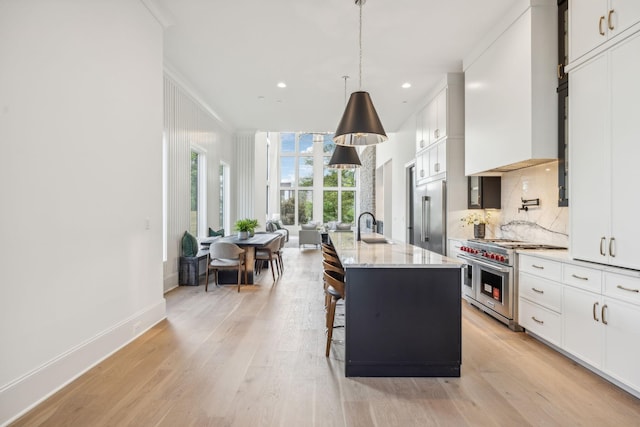 kitchen with white cabinets, light stone counters, high end appliances, and an island with sink