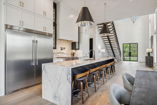 kitchen with a breakfast bar, a center island with sink, appliances with stainless steel finishes, decorative light fixtures, and light stone counters