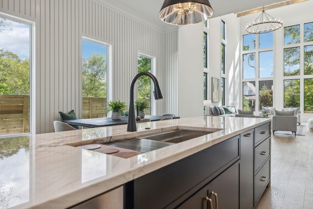 kitchen with sink, hanging light fixtures, light stone counters, a notable chandelier, and light hardwood / wood-style floors