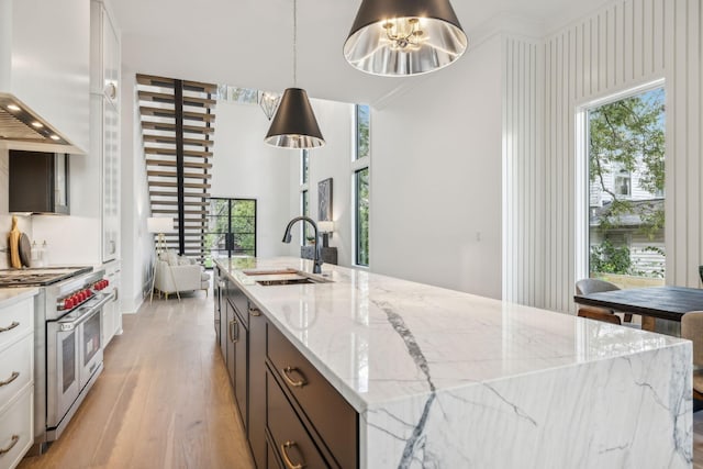 kitchen with custom exhaust hood, range with two ovens, sink, hanging light fixtures, and light stone counters